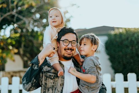 Father carrying two young children outdoors