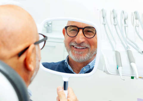 Older man checking his smile in a hand mirror